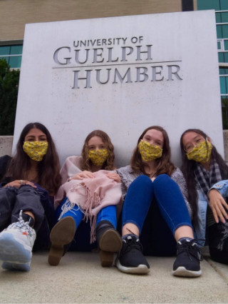 Four masked students sitting in front of Guelph-Humber building sign