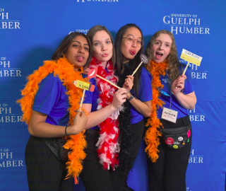 Four students in blue shirts wearing feather boas