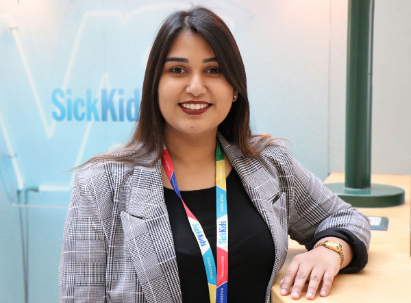 Woman in business attire with Sick Kids lanyard in front of wall with Sick Kids logo