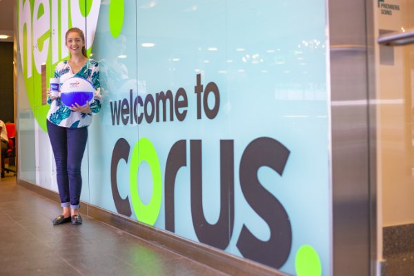 Student posing in front of wall with graphic: welcome to Corus