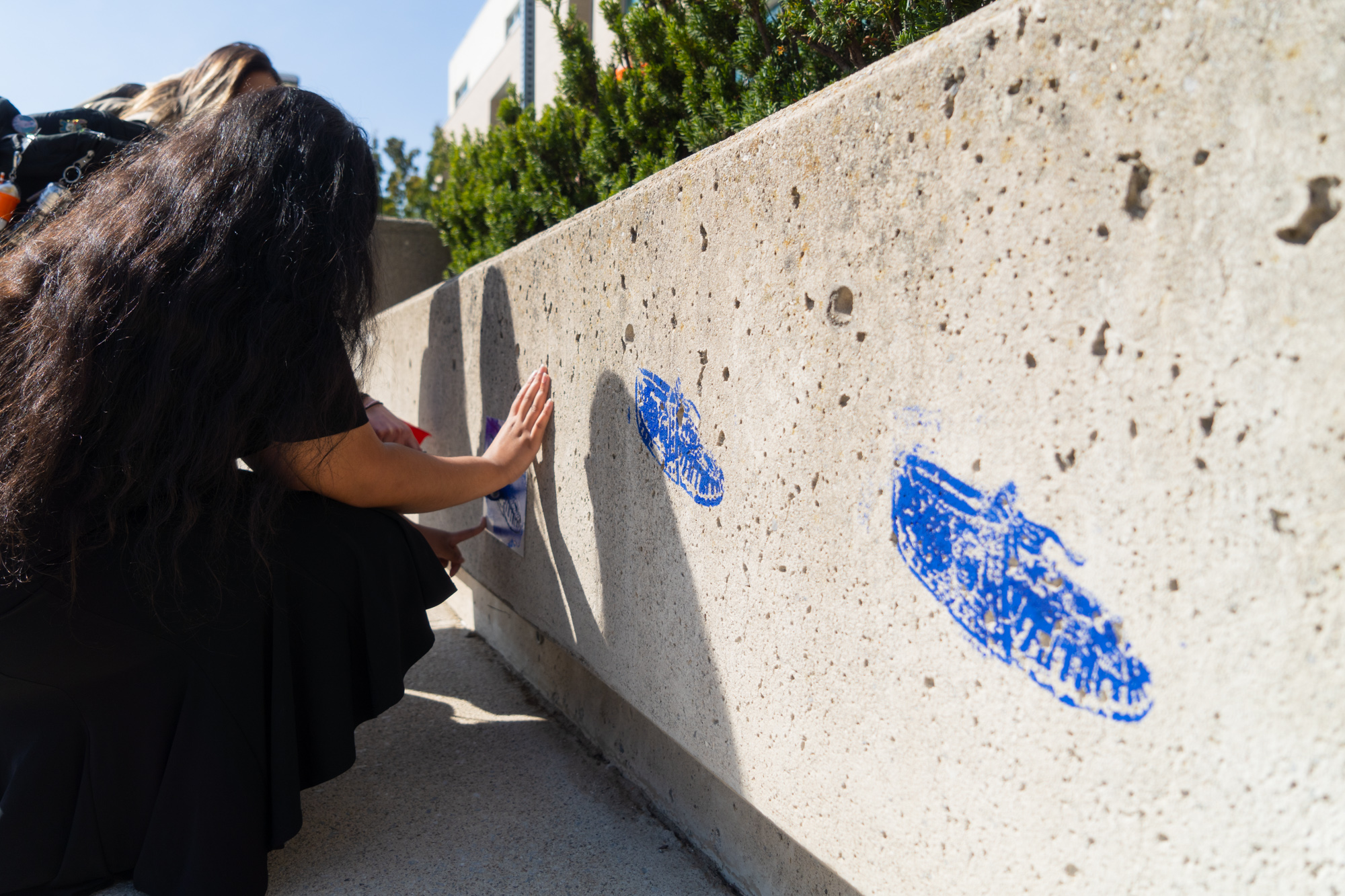A group of students are adding a third moccasin stencil onto a concrete wall while the first two painted stencils are in the foreground