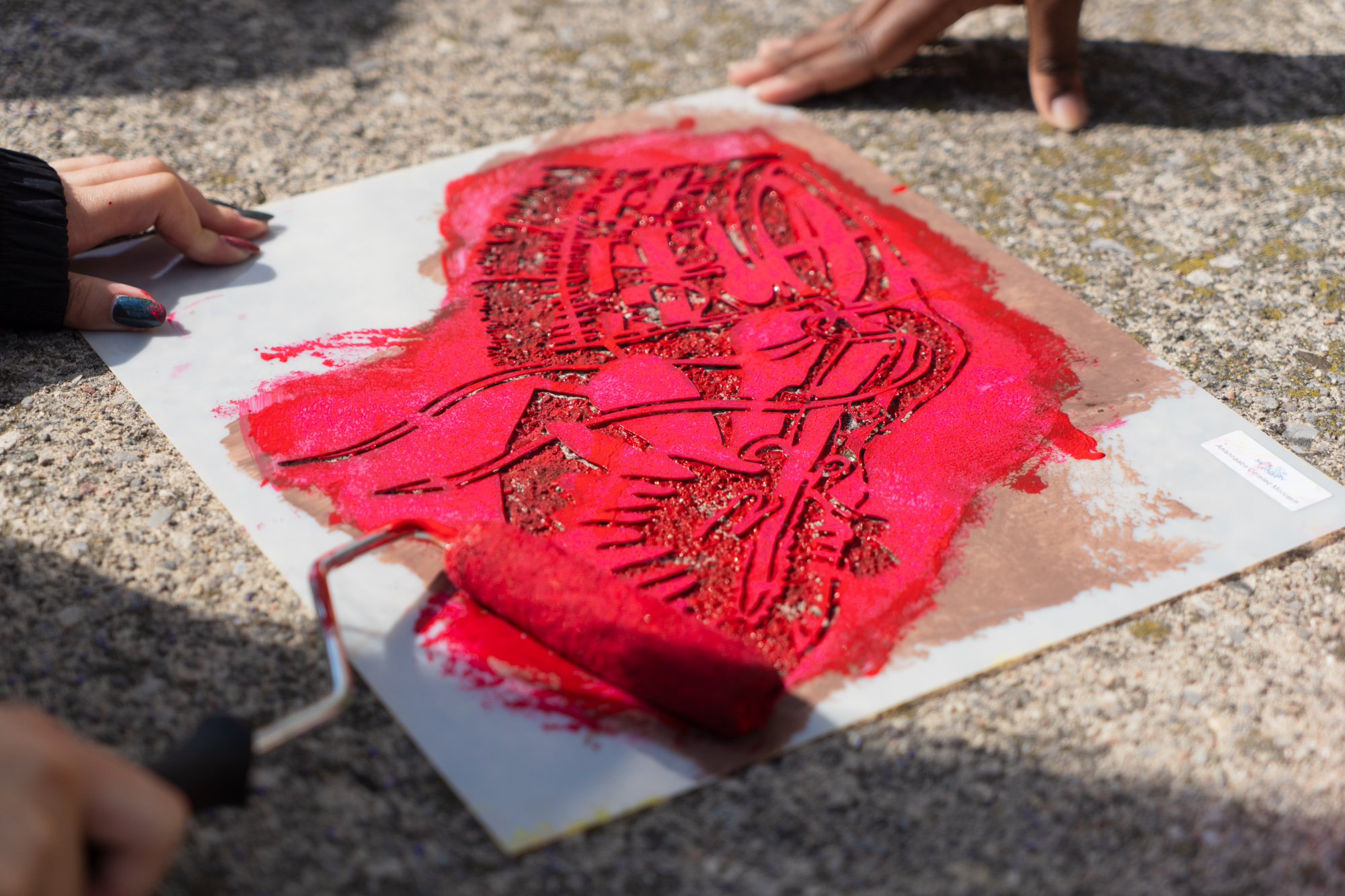A close up of a moccasin stencil while someone is rolling red paint over the stencil