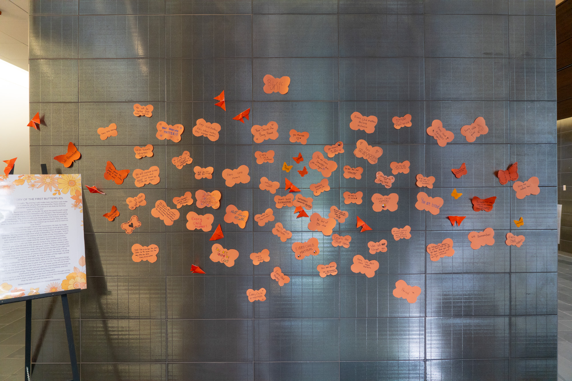 A wall with orange butterfly-shaped paper with written words and orange butterfly origami