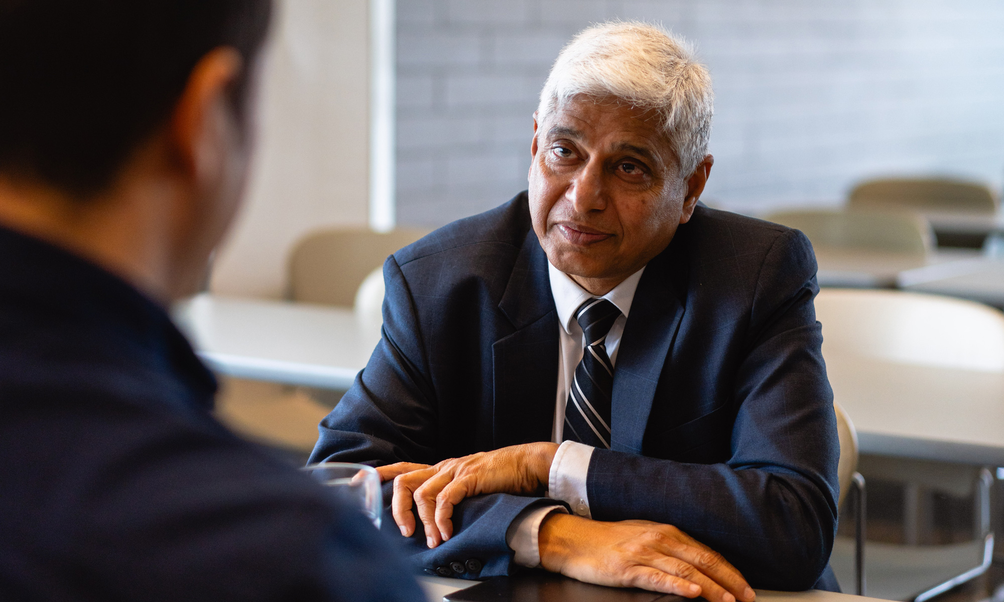 Vikas Swarup sitting with arms placed on top of each other, engaged in listening to someone speaking with him.