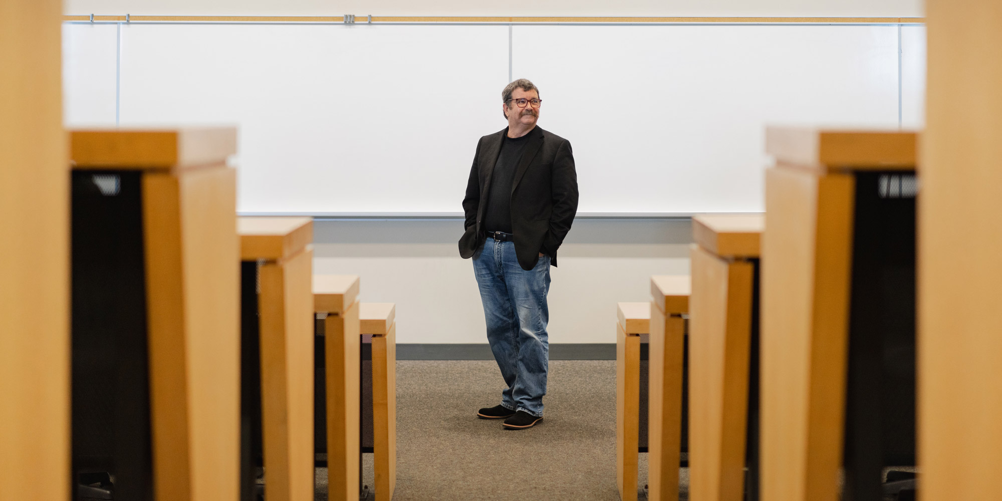 Glenn Hanna standing at the front of the classroom, framed by the aisle.