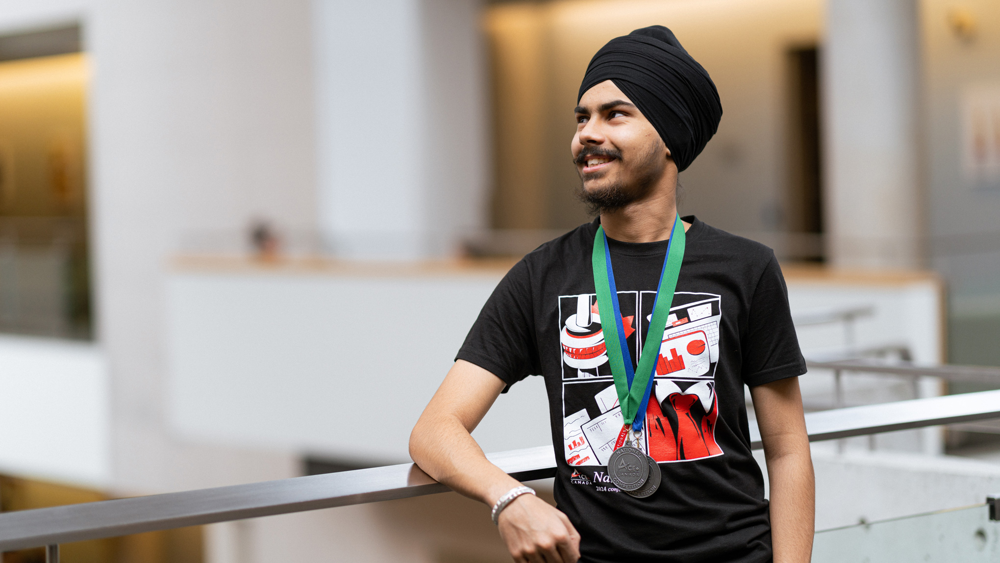 Nishan Athwal looking off-camera, smiling, while wearing two medals