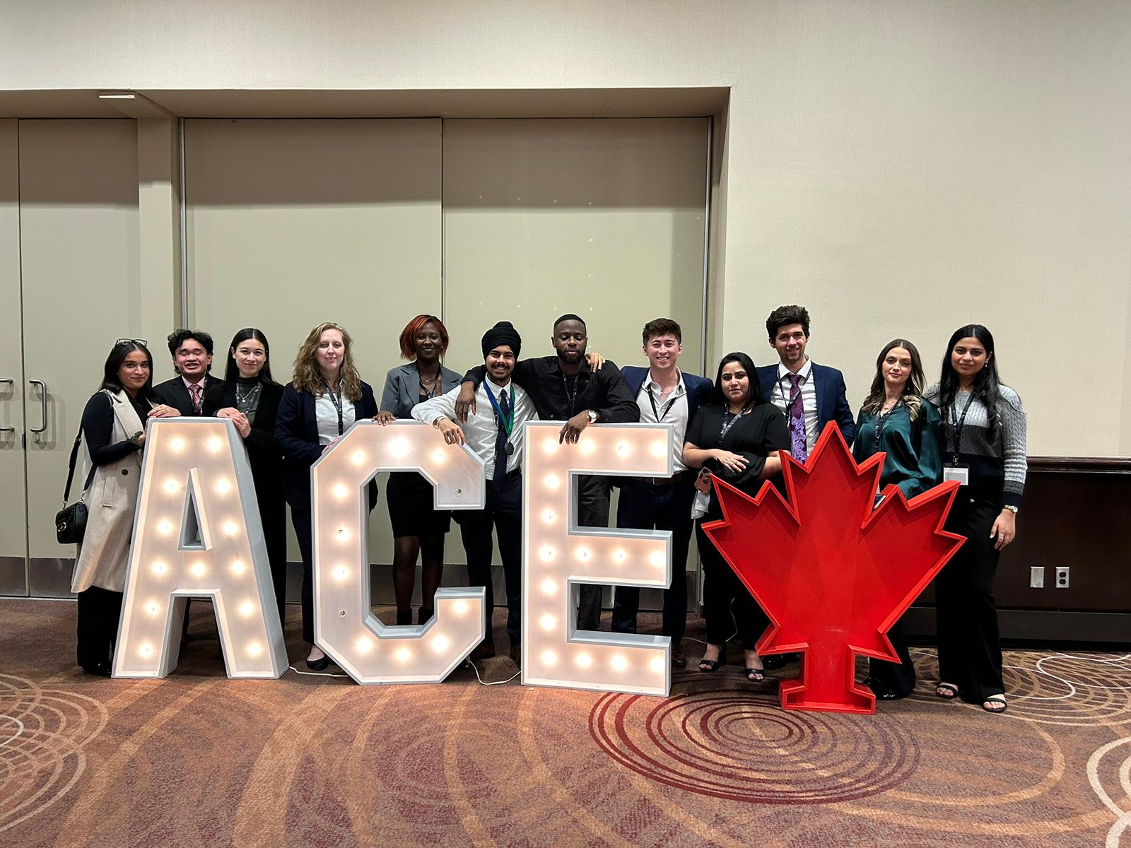Group photo of the members of ACE University of Guelph-Humber chapter in front of marquee signs spelling out ACE and a marquee sign of a maple leaf