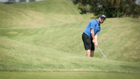 Photo of UofGH alumni hitting golf ball from behind grassy hill