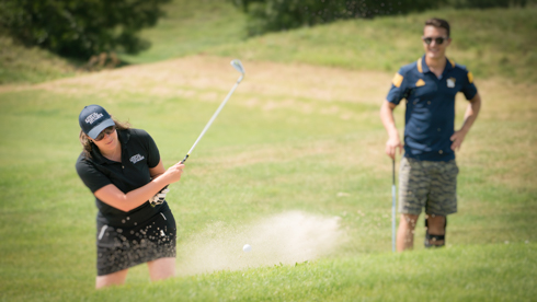 Photo of UofGH Program Head hitting golf ball out of sand trap