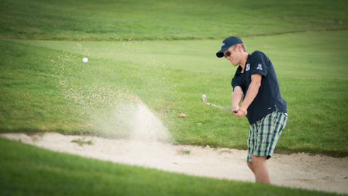 Photo of UofGH alumni hitting golf ball out of sand trap