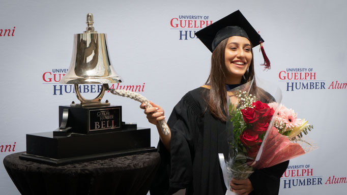 A graduate poses with the UofGH bell