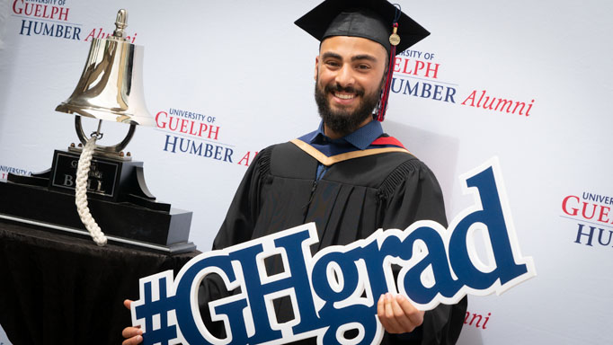 A graduate holds up a sign reading "GH Grad"