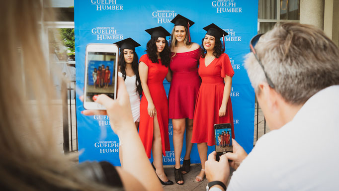 Four graduates posing in front of a blue UofGH backdrop
