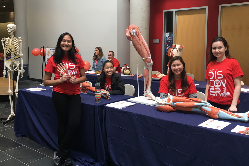 Student volunteers smile beside an anatomical model