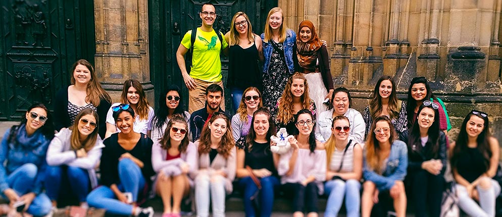 The Study Abroad group sits in front of a Czech building, holding Tikko.