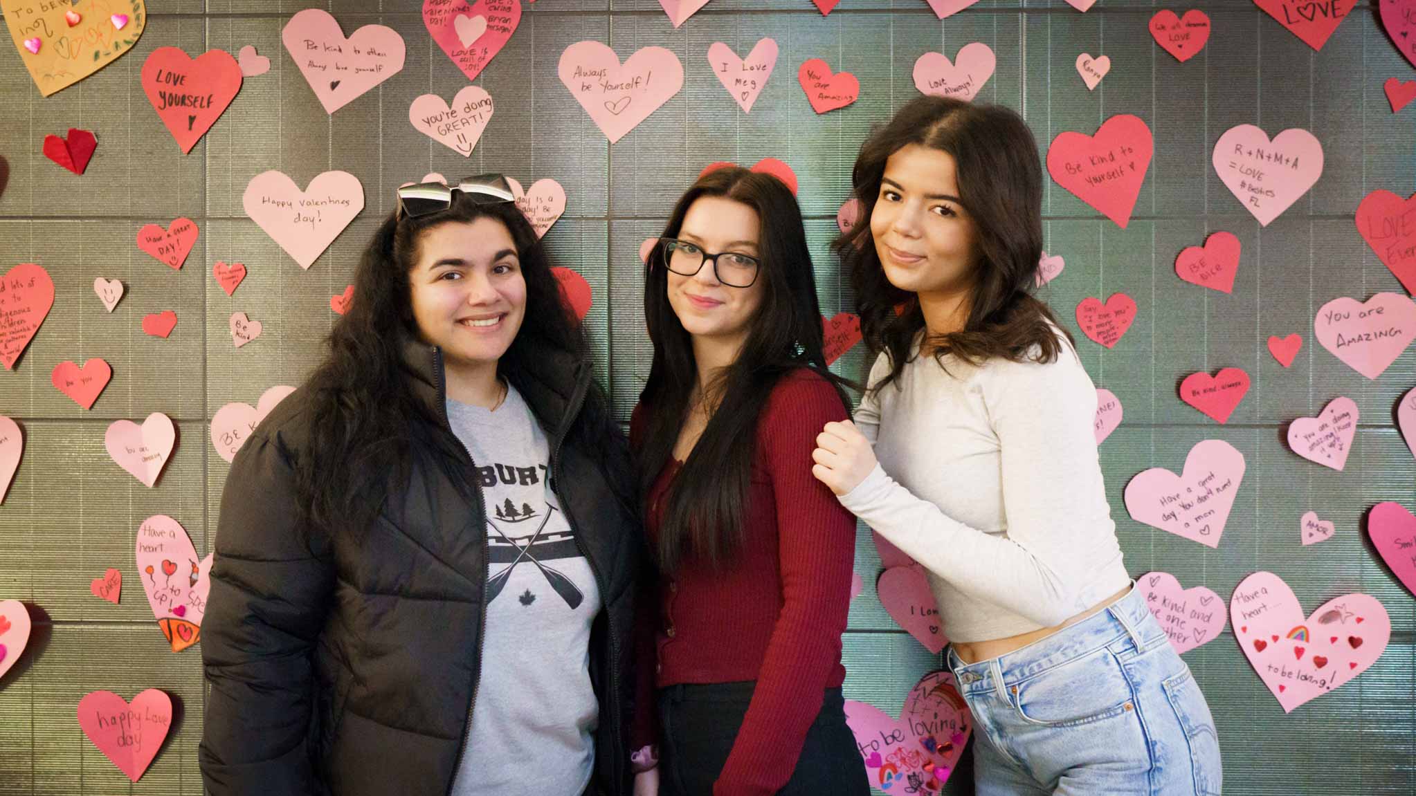 Students stand in front of wall covered in paper hearts