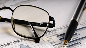 An image of glasses and a pen over the newspaper