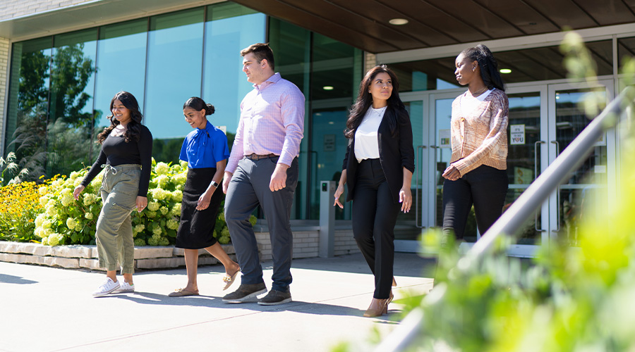 Five individuals walking away from a building while talking to one another