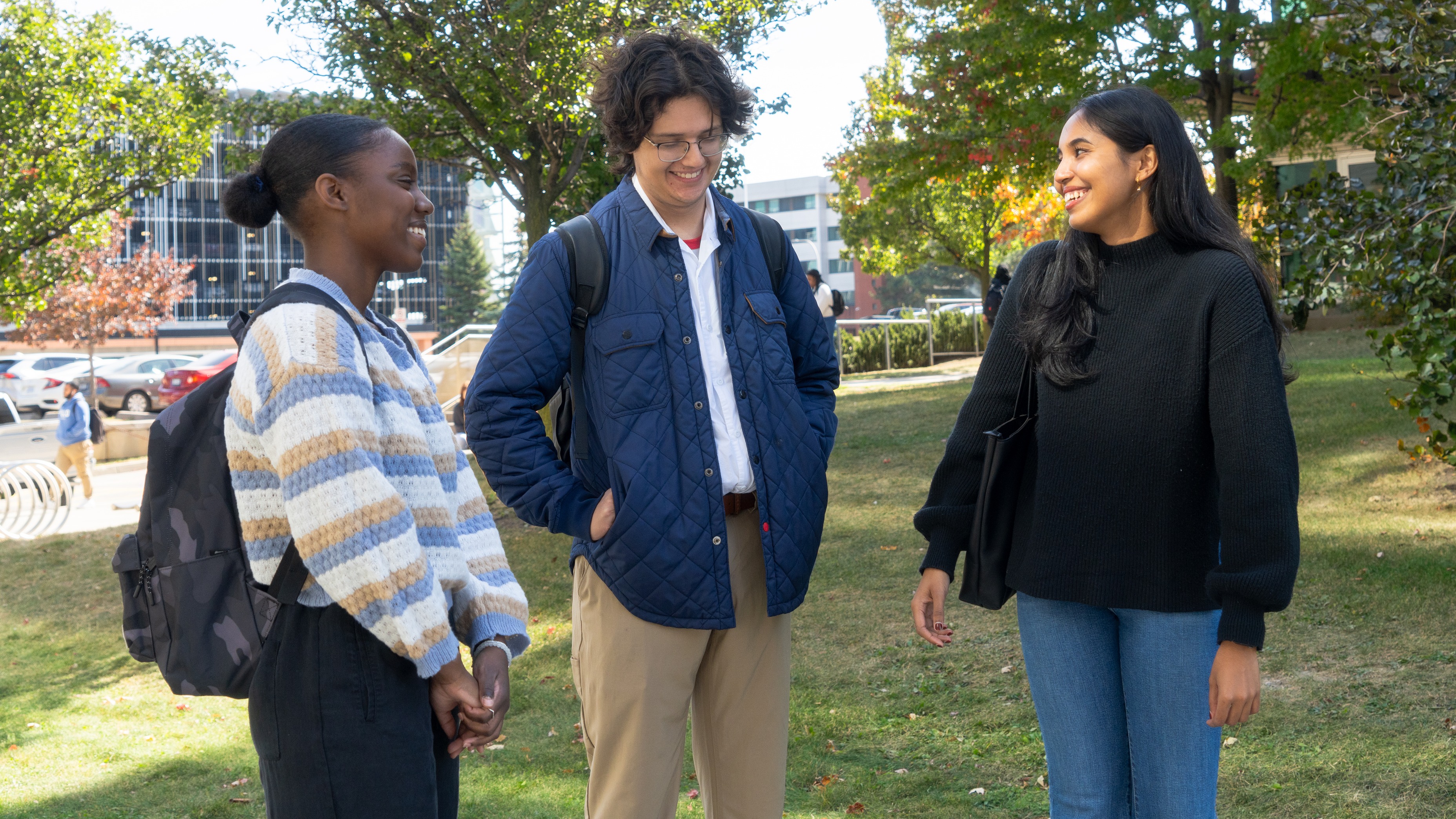 three students standing chatting outside on the grass