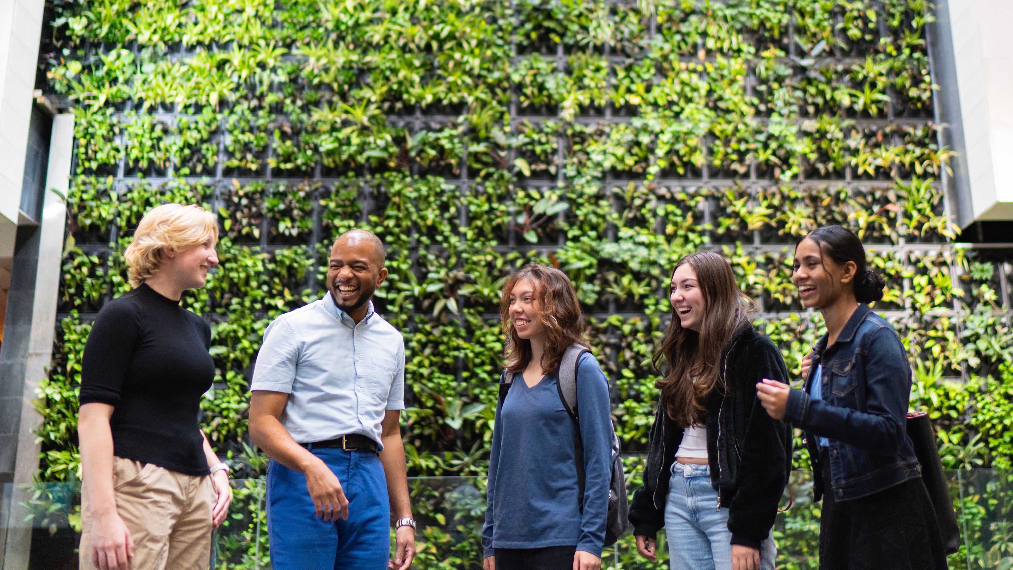 Five students standing in front of plant wall