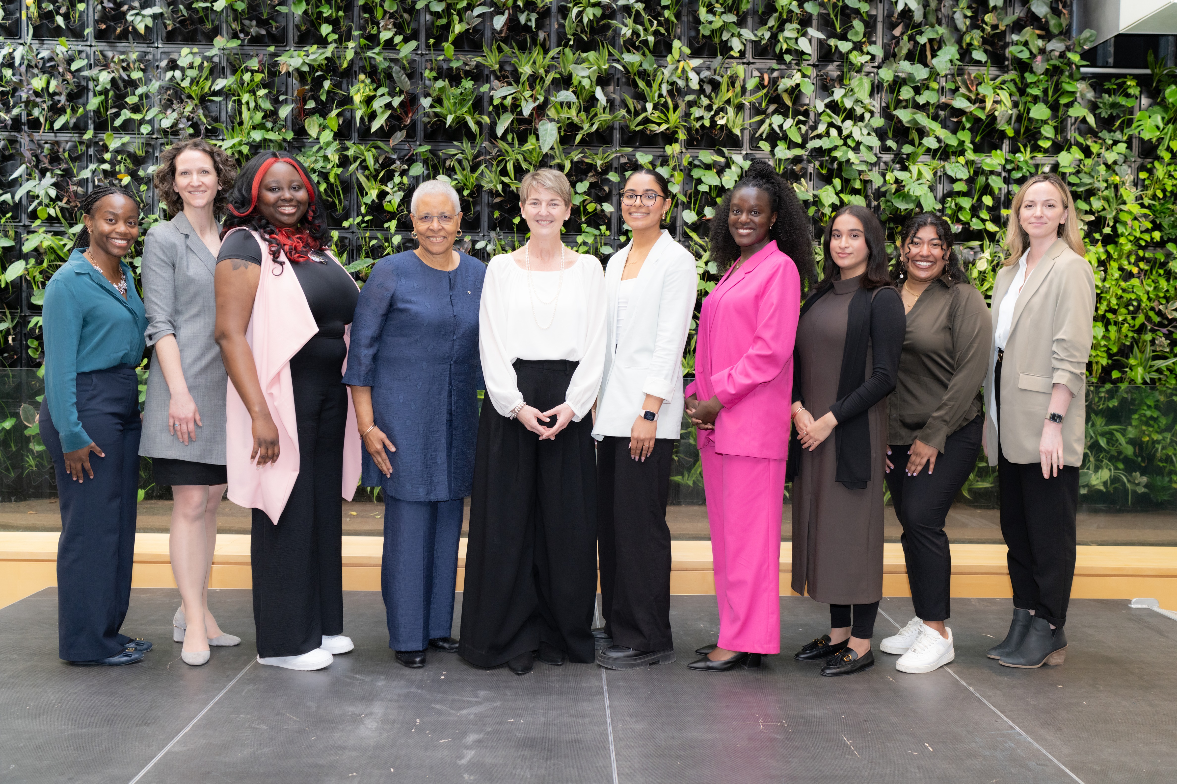 Ten women from the 2024 GH Women of Distinction event posing in front of a plant wall