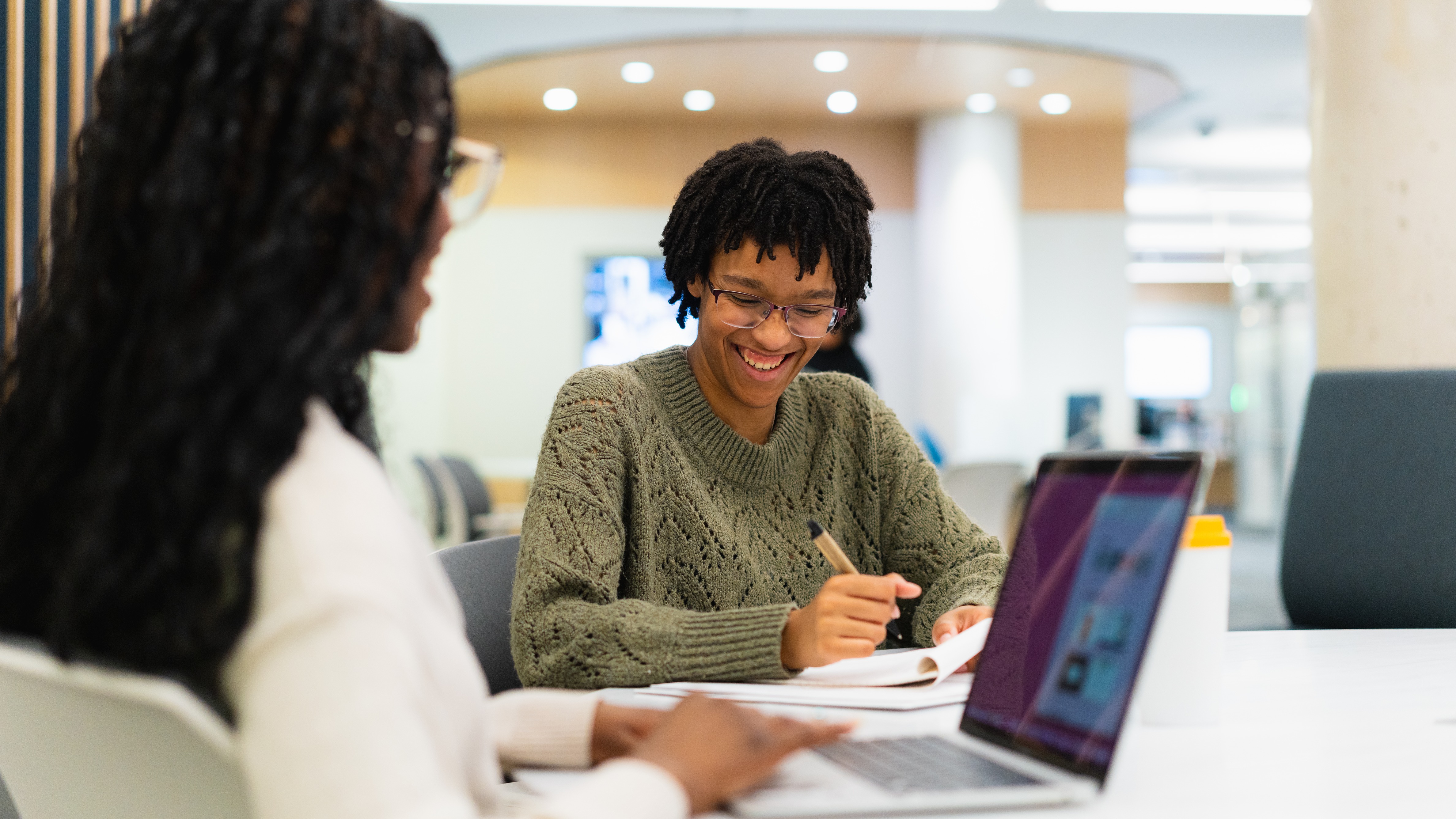 Two students at a desk with computers one smiling