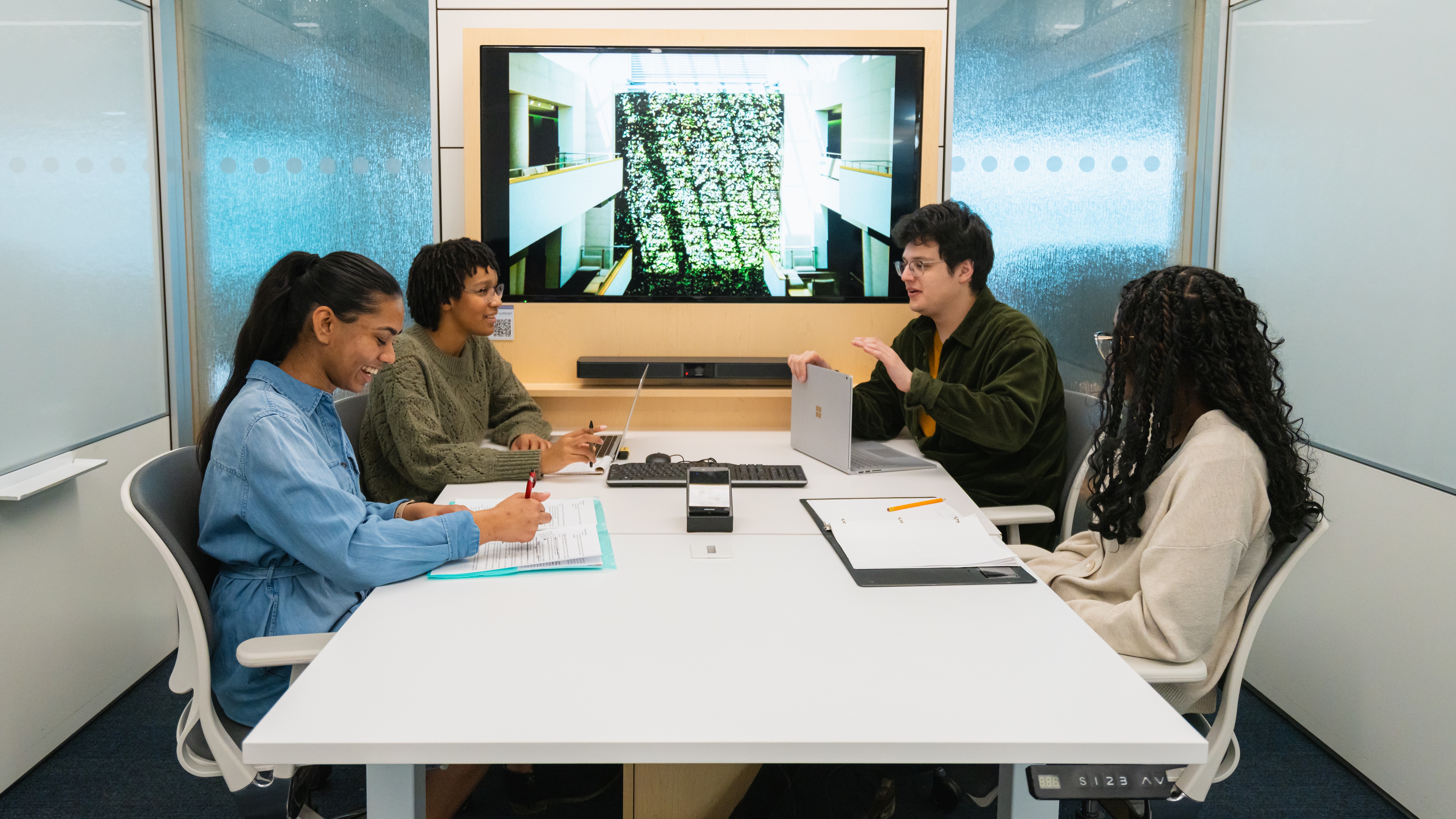 Four students working at a learning commons desk with a screen behind them