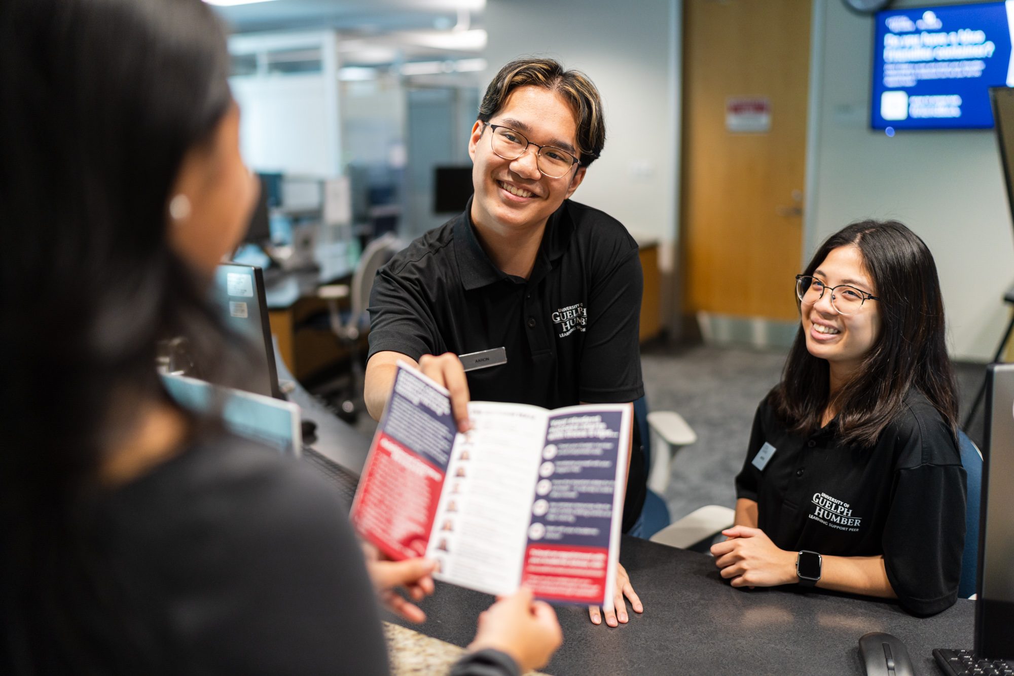 Two people helping a student while pointing at a brochure