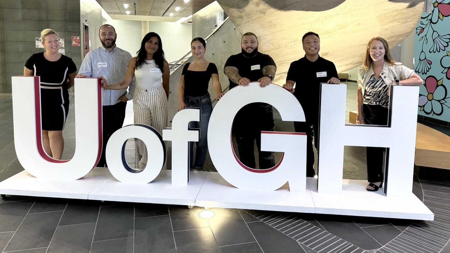 Group of people behind large UofGH sign