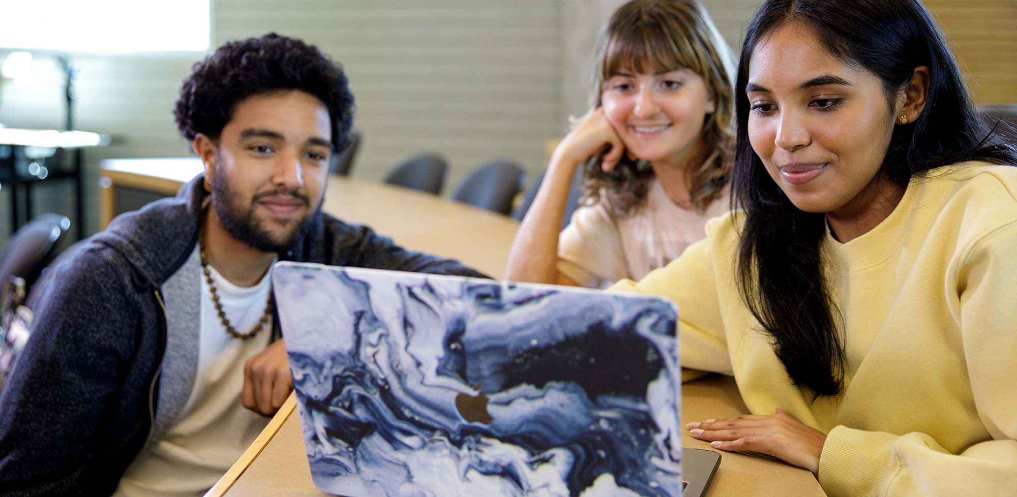Three students look at files on a laptop in a classroom