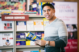 Smiling student holding a book in front of the Career Services sign