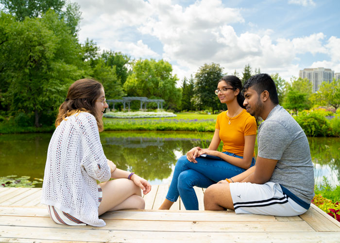 Three people sitting near pond