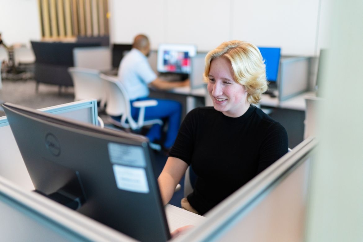 student sitting in front of computer screen smiling