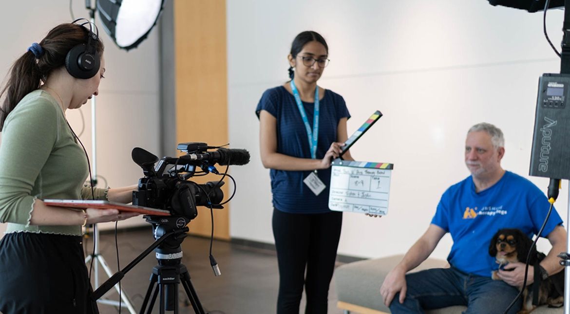 Two students filming a man with his therapy dog