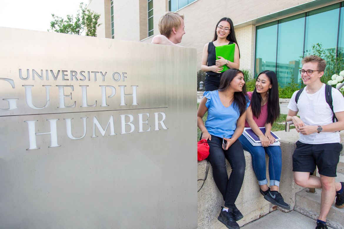 students chatting next to u of gh sign