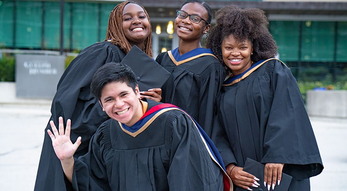 four grads in gowns waving and smiling