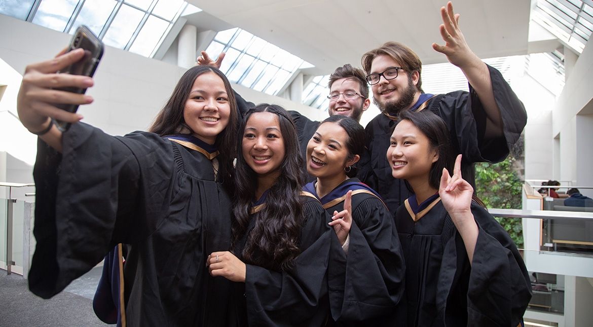 six students in grad gowns taking a selfie