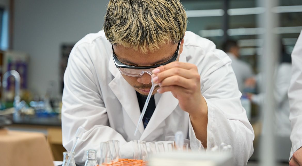 Male student in lab coat with dropper and test tubes