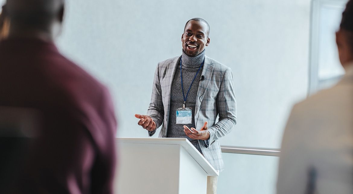 man wearing a suit at podium speaking to audience