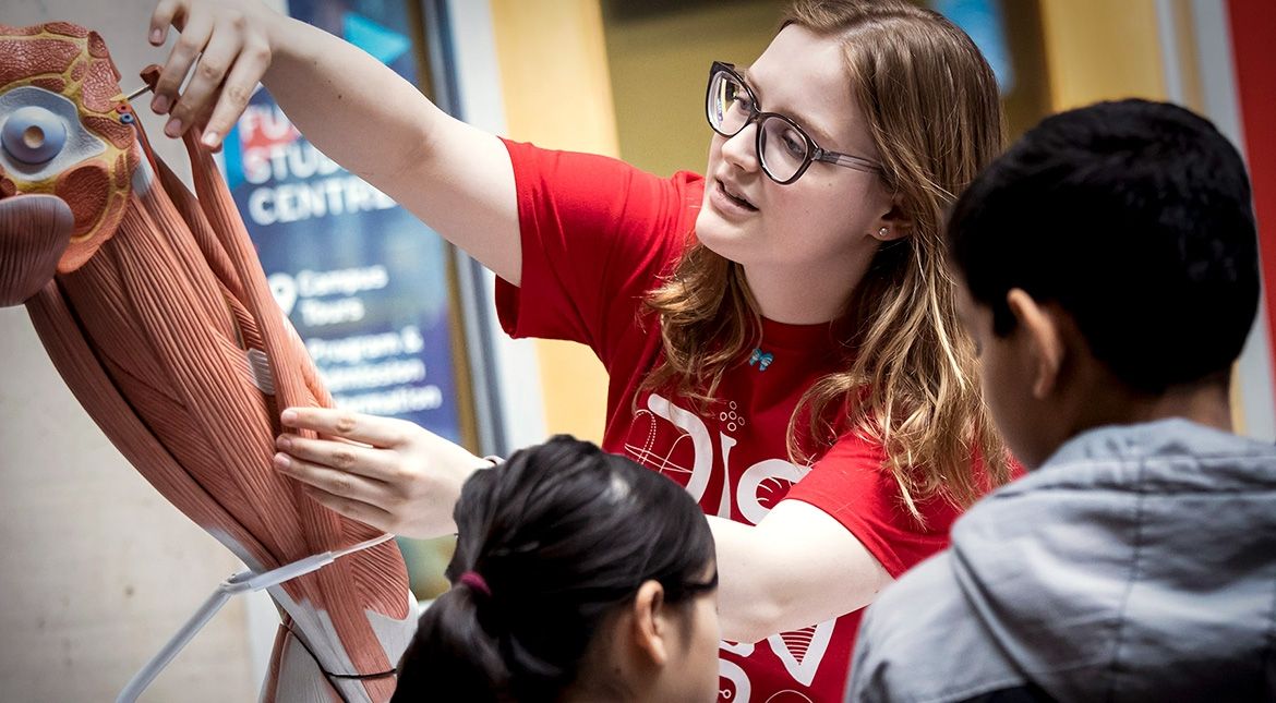Female student showing two kids a muscle display