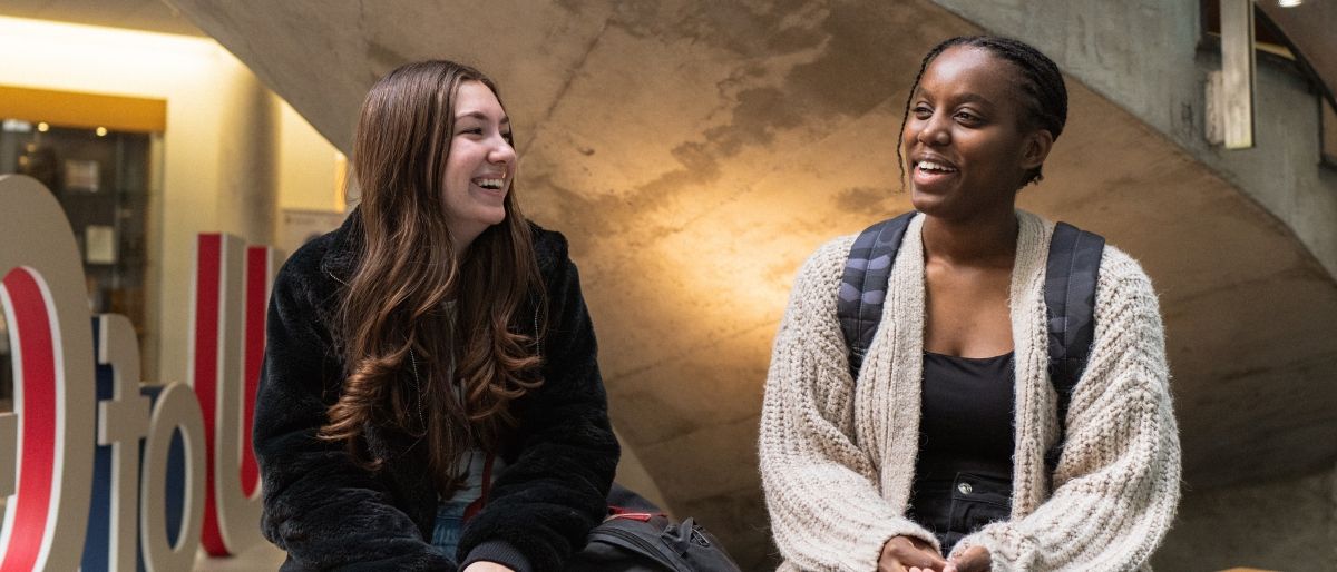 Two students sitting on a bench talking and smiling