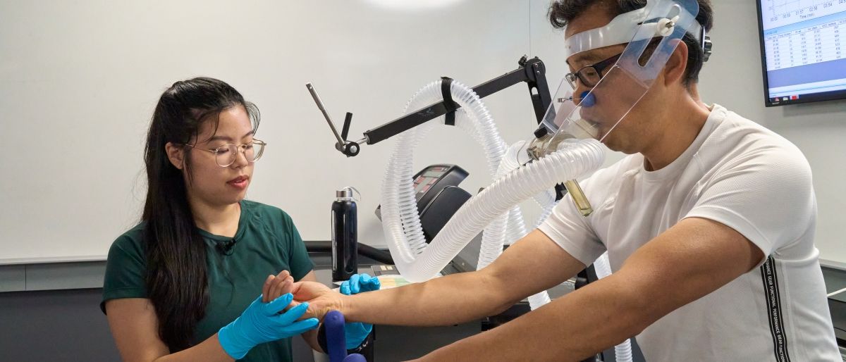 Kinesiology banner man on bike while student takes blood pressure