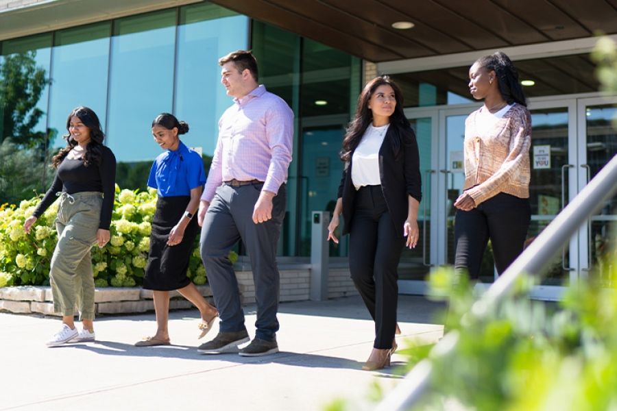 Five individuals walking away from a building while talking to one another