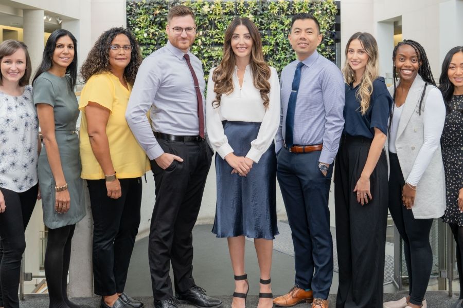 A group of nine academic advisors posing with the plant wall in the background