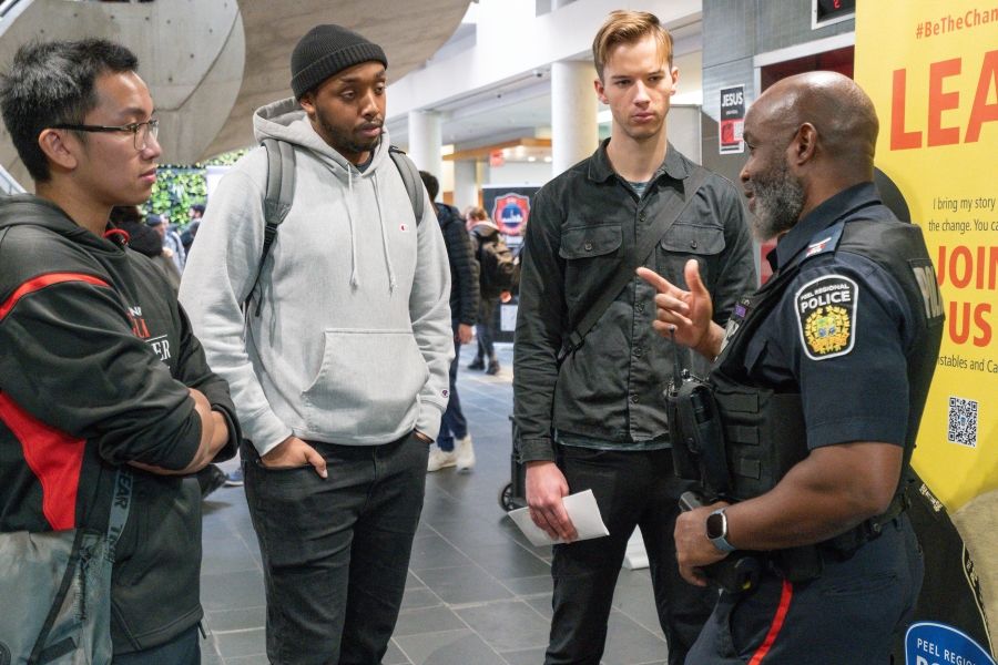 Three students standing speaking with a police officer at a career fair
