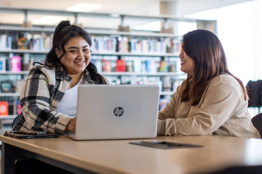 Two women in front of a laptop with library stacks in the background