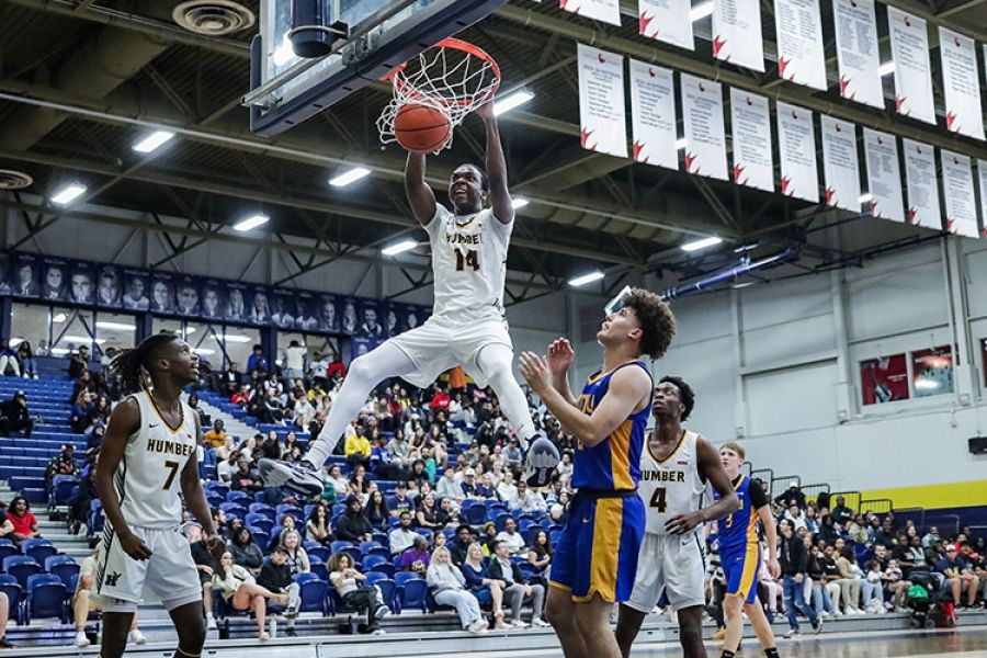 A student-athlete doing a slam dunk while two teammates and an opponent watch on