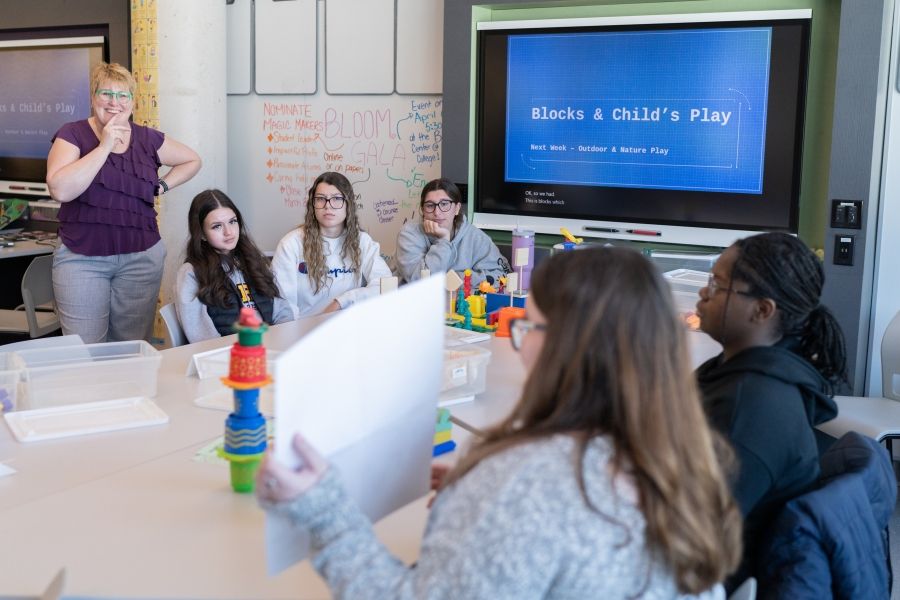 Instructor with a group of students at a desk with a screen