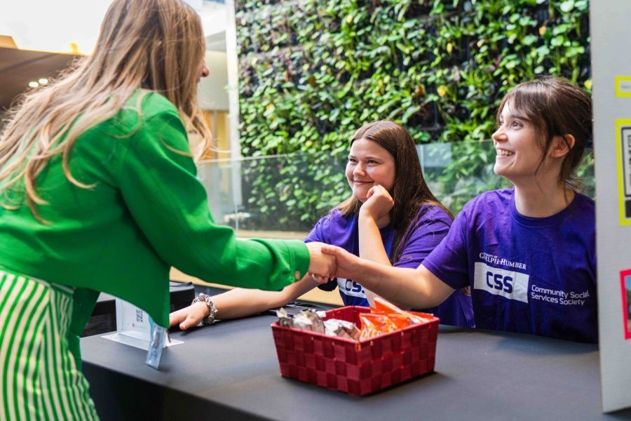 Two individuals shaking hands while another person is looking on smiling