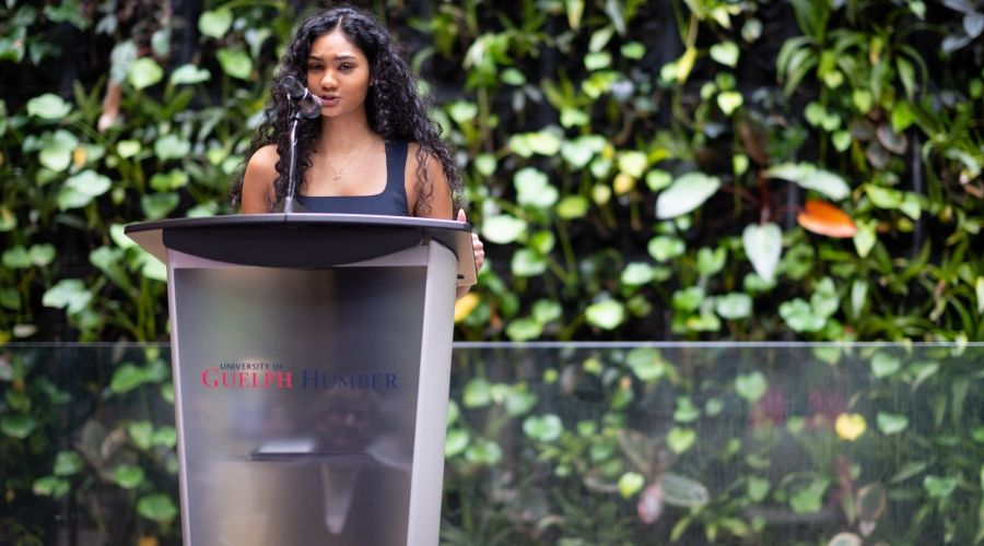 Someone at a podium speaking with a plant wall behind them